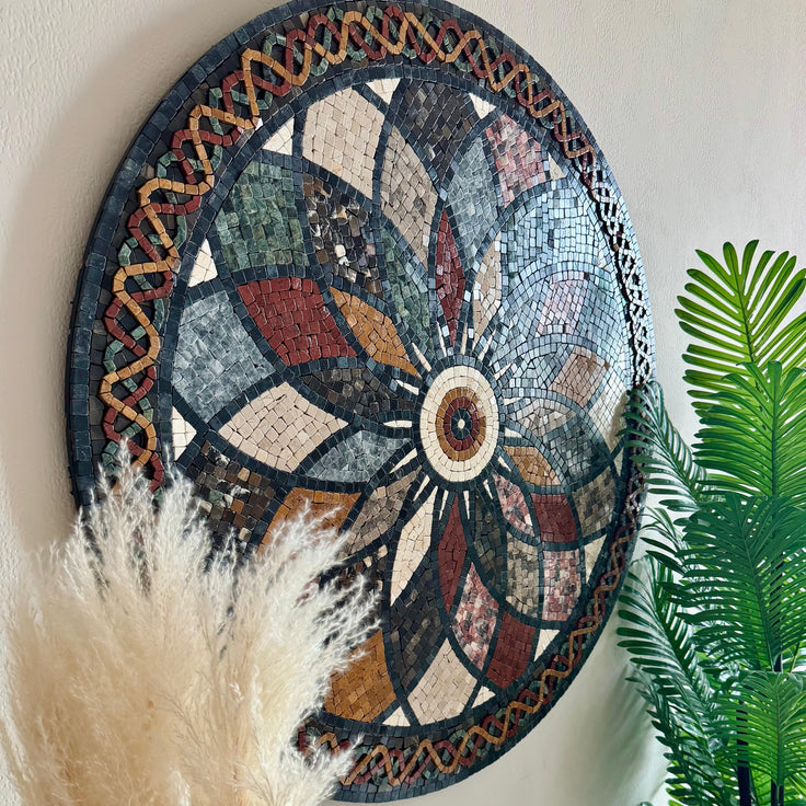 Round stone mosaic floral rosette wall art with multicolor tiles; feather and palm leaves nearby